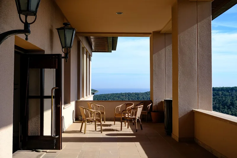 Sunny Parador terrace with wicker chairs overlooking forest and sea