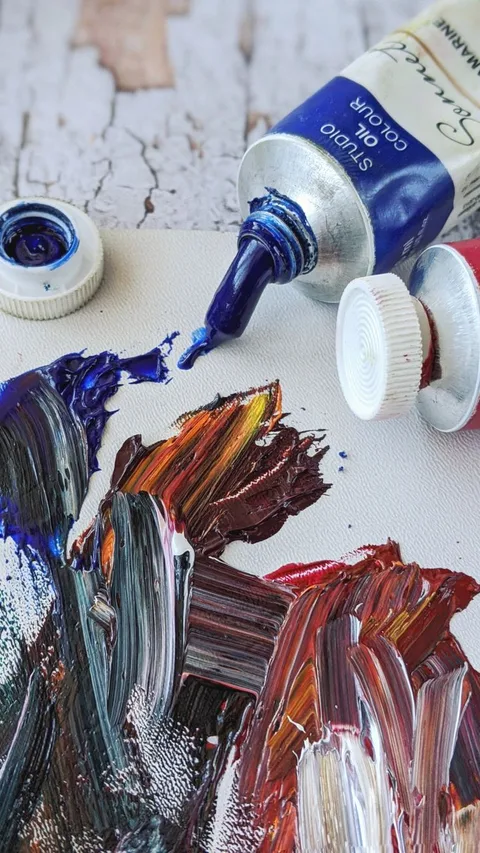 Close-up of vibrant oil paint tubes and brush strokes on canvas, capturing creativity.