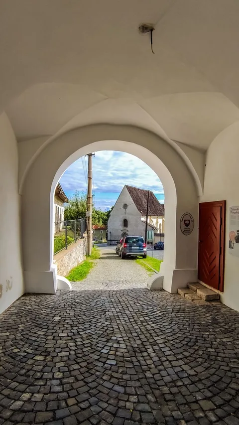 A view through an archway revealing a cobblestone street and picturesque village.