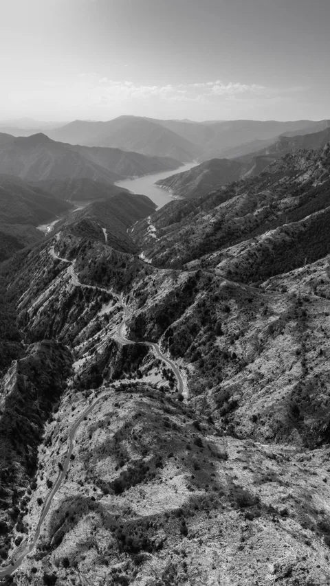 Explore the rugged mountain ranges with winding roads under a clear sky in black and white.