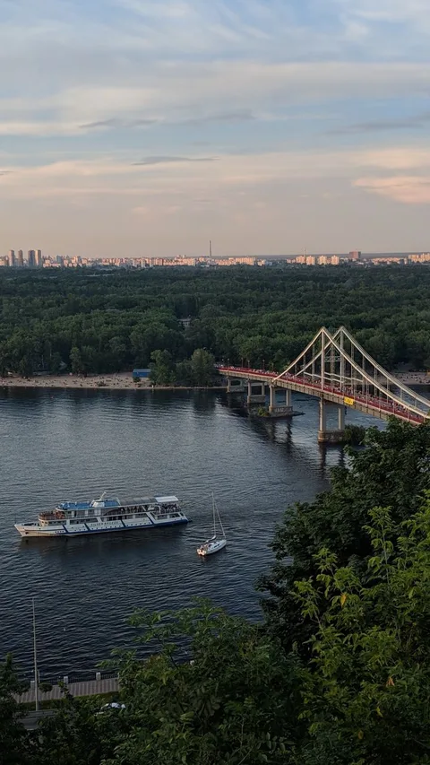 Scenic aerial view of the Pedestrian Bridge over the Dnieper River in Kyiv with boats cruising below.