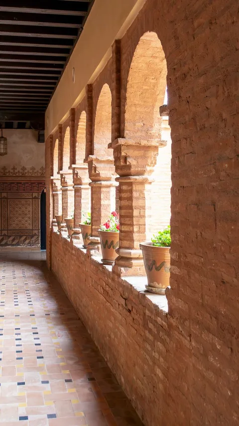 Sunlit brick archway featuring terracotta flower pots with vibrant blooms.