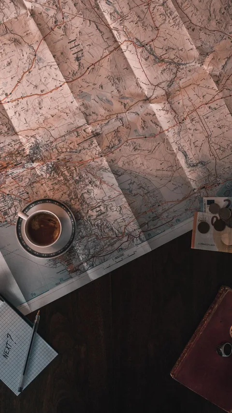 Flat lay of map, coffee, coins, and notebook for travel planning.