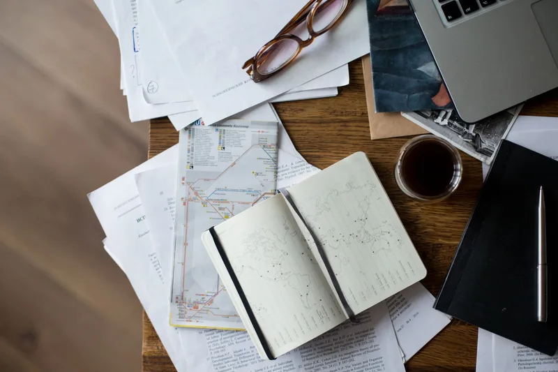 Open travel notebook with maps and coffee planning a 7-day Parador trip budget